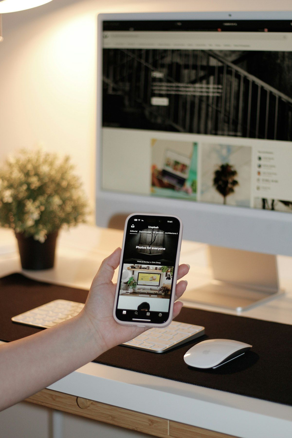 Hand holding a phone with a desktop monitor visible in the background