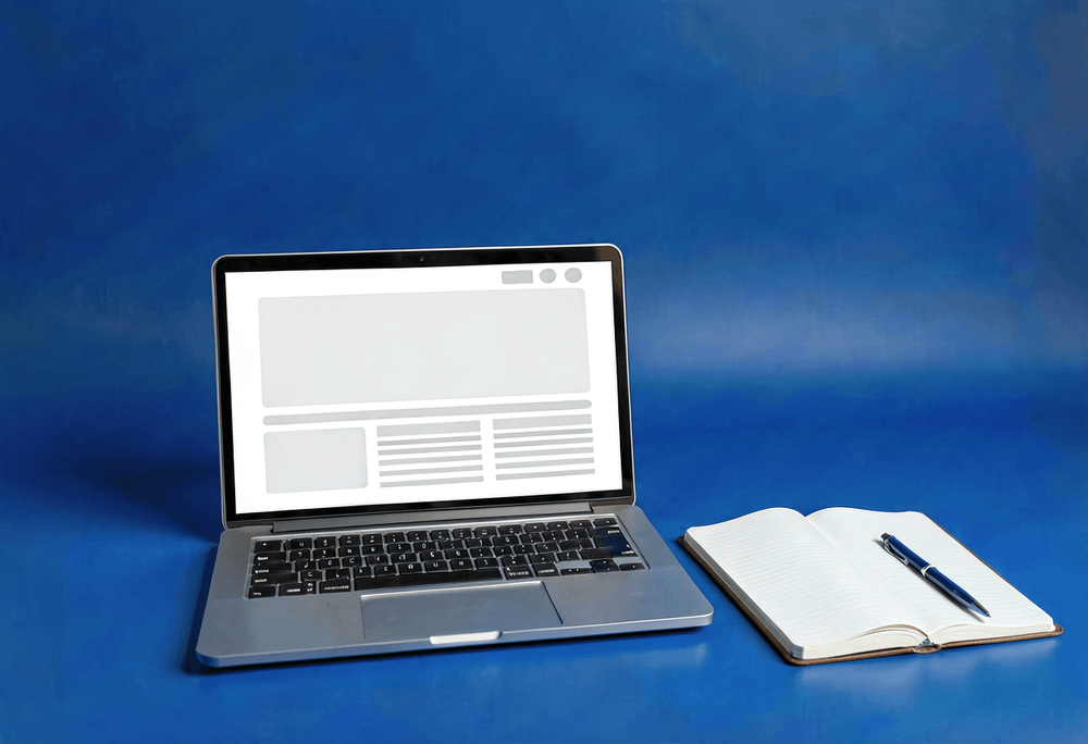Open laptop showing blog layout with open notebook and pen on blue studio background